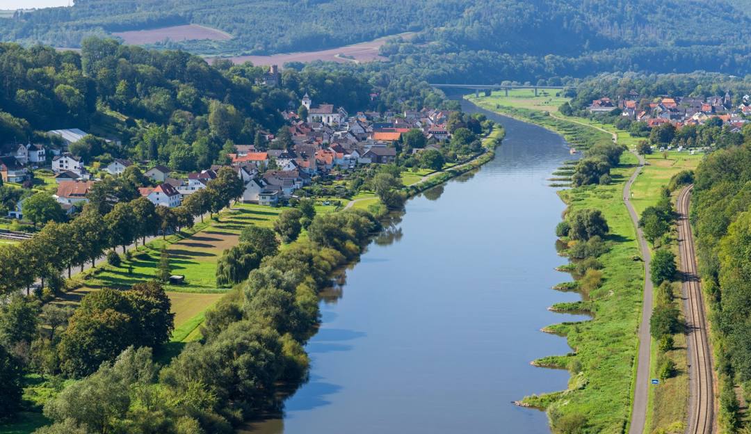 Wesertal in der Vogelperspektive: Fluss, Ufer und Ortschaft zwischen grünen Hügeln.