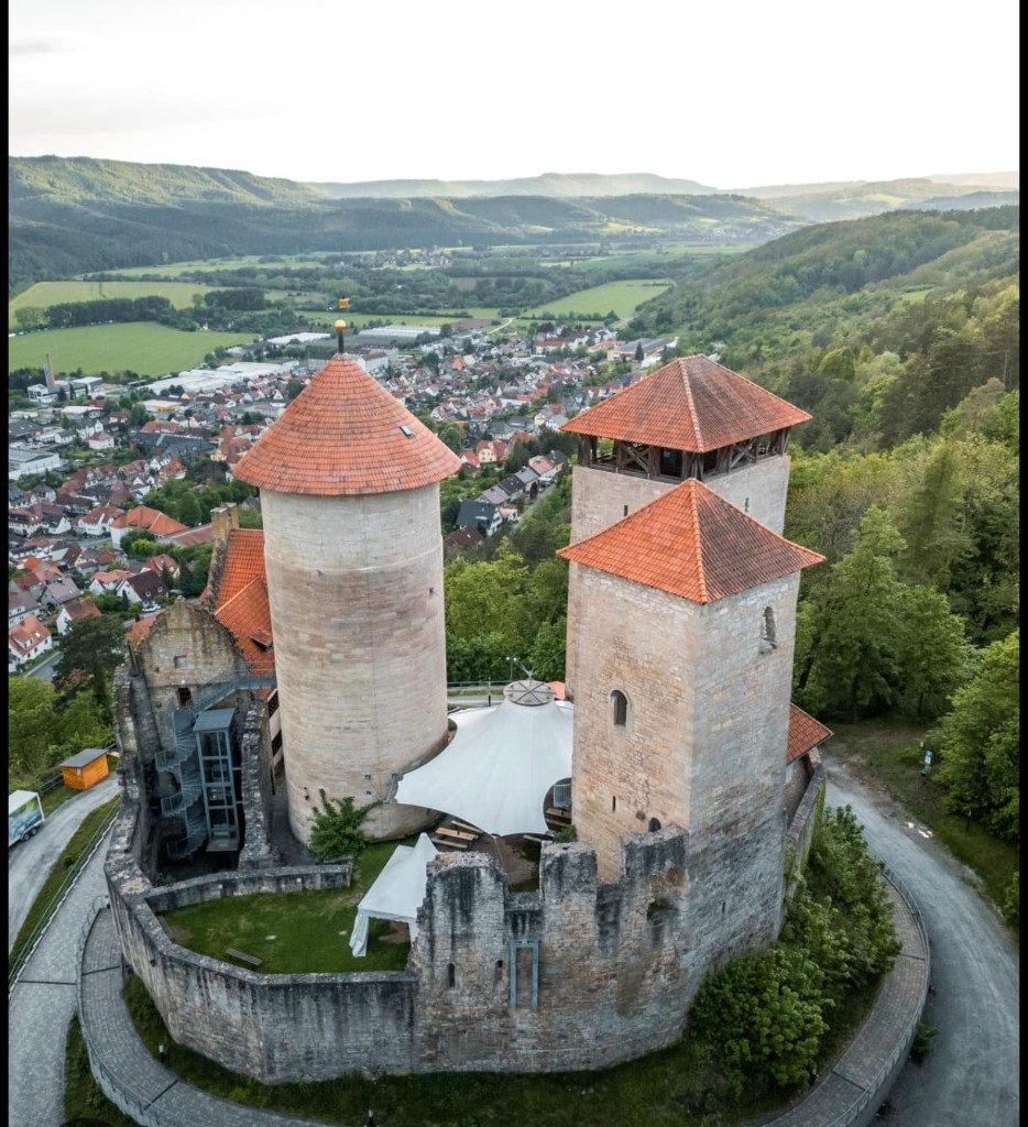 Burganlage mit roten Dächern auf einem Hügel und weitem Blick über das Tal.